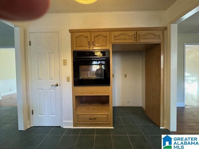 kitchen with light brown cabinetry, black oven, a textured ceiling, and dark tile patterned floors