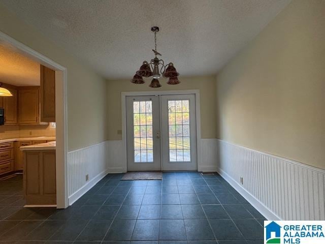 entryway with a textured ceiling, a chandelier, dark tile patterned flooring, and french doors