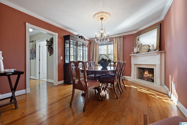 dining room with a fireplace, crown molding, a chandelier, and light wood-type flooring