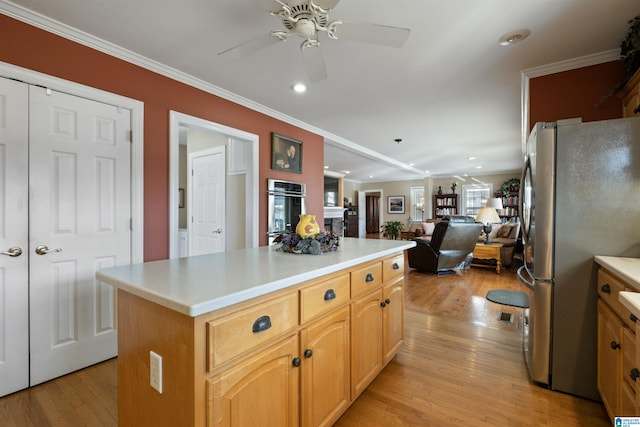 kitchen with crown molding, appliances with stainless steel finishes, a kitchen island, light hardwood / wood-style flooring, and ceiling fan