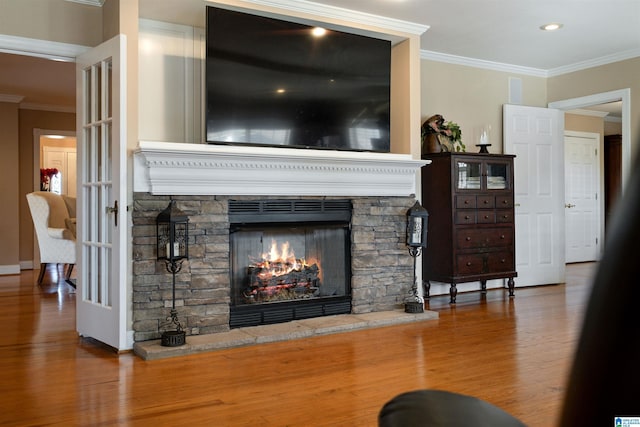 living room featuring wood-type flooring, ornamental molding, and a stone fireplace