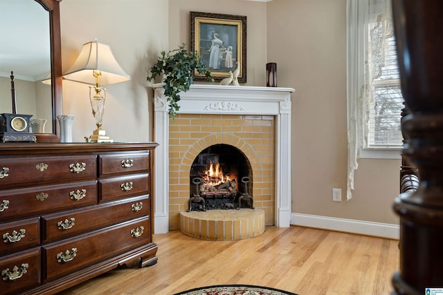 living area featuring light hardwood / wood-style floors, ornamental molding, and a brick fireplace