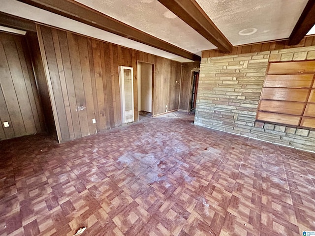 unfurnished living room featuring wood walls, parquet flooring, a textured ceiling, and beam ceiling