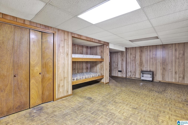 basement featuring parquet flooring, wooden walls, heating unit, and a drop ceiling