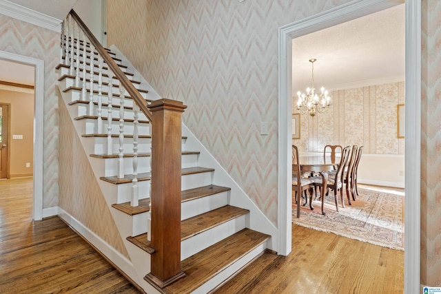 stairs with wood-type flooring, a chandelier, and ornamental molding