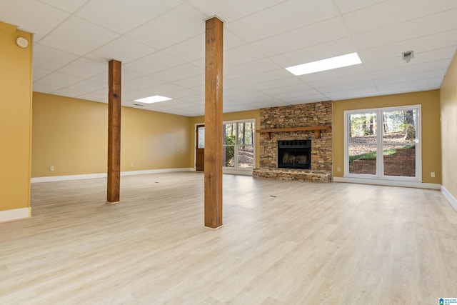 unfurnished living room with light hardwood / wood-style floors, a drop ceiling, and a stone fireplace