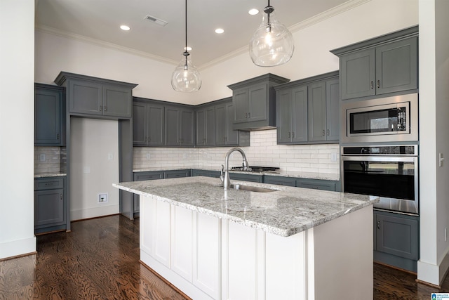 kitchen with sink, decorative light fixtures, ornamental molding, stainless steel appliances, and a center island with sink