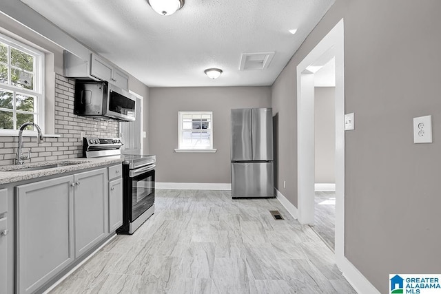 kitchen with decorative backsplash, sink, stainless steel appliances, light stone counters, and gray cabinets