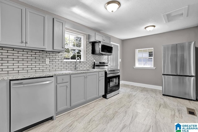 kitchen with sink, tasteful backsplash, light stone countertops, gray cabinets, and stainless steel appliances