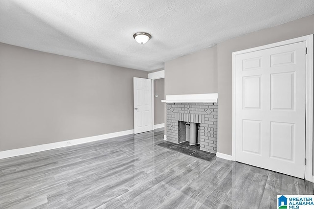 unfurnished living room featuring a brick fireplace, hardwood / wood-style floors, and a textured ceiling