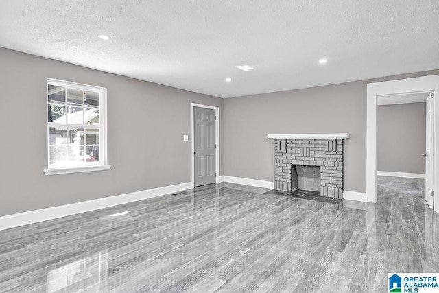 unfurnished living room featuring light wood-type flooring, a brick fireplace, and a textured ceiling