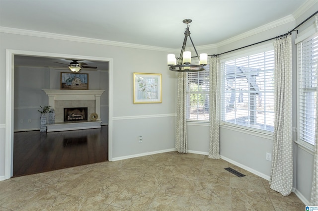 unfurnished dining area featuring crown molding, plenty of natural light, ceiling fan with notable chandelier, and a fireplace