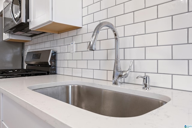 kitchen with sink, light stone counters, white cabinetry, appliances with stainless steel finishes, and decorative backsplash