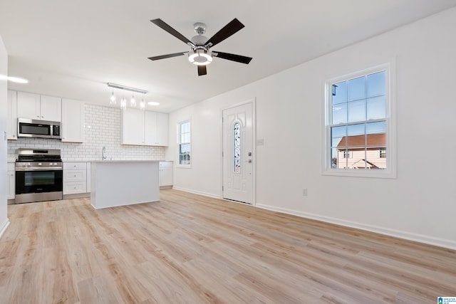 kitchen with white cabinetry, tasteful backsplash, light wood-type flooring, pendant lighting, and stainless steel appliances