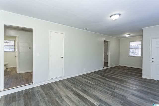 unfurnished bedroom featuring dark wood-type flooring, multiple windows, and ensuite bath