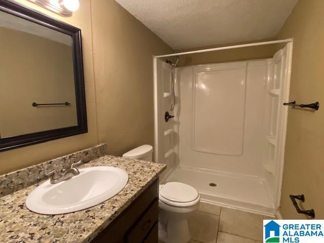 bathroom with toilet, a textured ceiling, walk in shower, tile patterned floors, and vanity