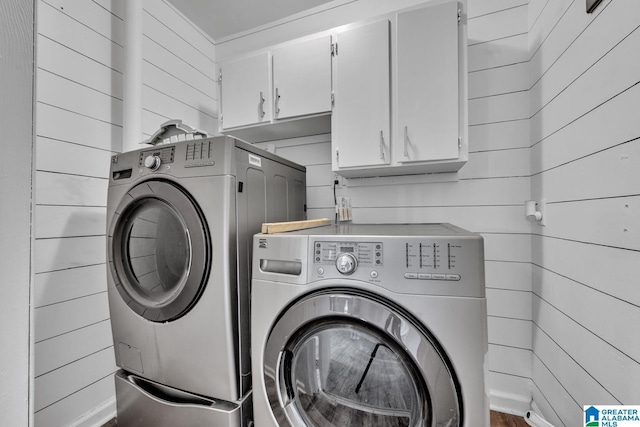 clothes washing area with washer and clothes dryer, wooden walls, and cabinets