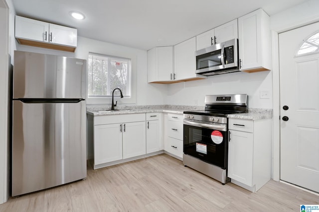 kitchen with light hardwood / wood-style floors, white cabinetry, light stone counters, and appliances with stainless steel finishes