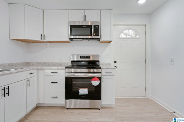 kitchen featuring white cabinets, stainless steel appliances, light stone countertops, and light wood-type flooring