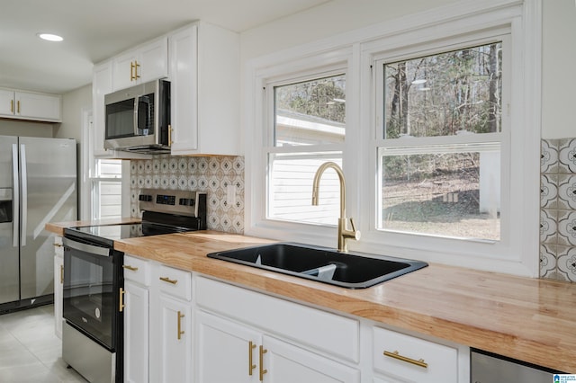 kitchen with appliances with stainless steel finishes, sink, white cabinetry, butcher block countertops, and decorative backsplash