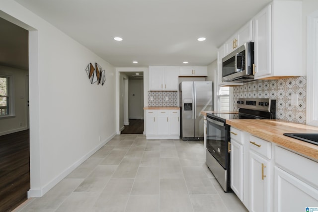 kitchen with appliances with stainless steel finishes, backsplash, white cabinets, light tile patterned flooring, and butcher block counters