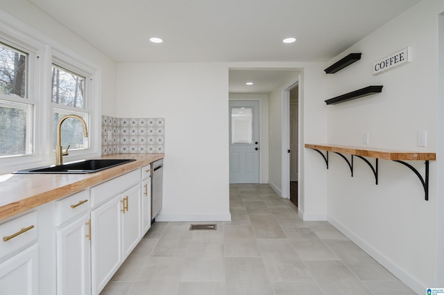 kitchen featuring white cabinets, wood counters, sink, backsplash, and stainless steel dishwasher