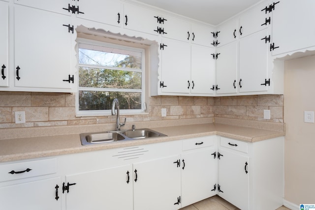 kitchen with sink, backsplash, white cabinets, light tile patterned floors, and ornamental molding