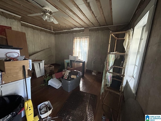 misc room with ceiling fan, wooden walls, and dark wood-type flooring