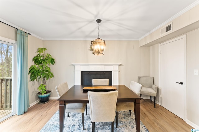 dining space with ornamental molding, an inviting chandelier, and light wood-type flooring