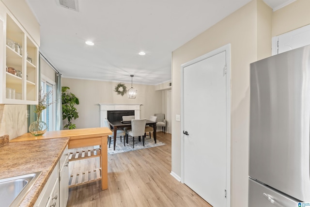 kitchen featuring stainless steel refrigerator, white cabinetry, hanging light fixtures, light hardwood / wood-style floors, and a chandelier