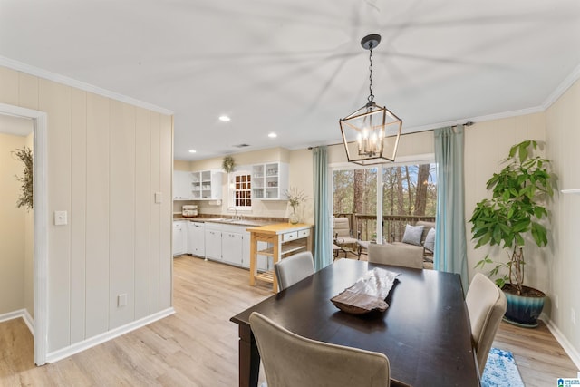 dining space featuring crown molding, an inviting chandelier, sink, and light hardwood / wood-style flooring