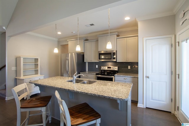 kitchen featuring pendant lighting, sink, appliances with stainless steel finishes, light stone counters, and an island with sink