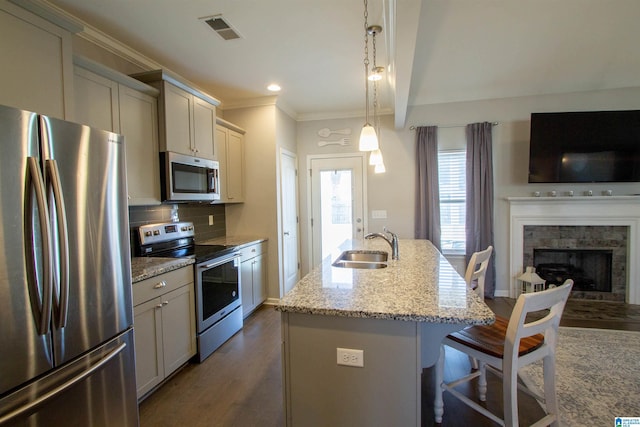 kitchen with sink, hanging light fixtures, a center island with sink, stainless steel appliances, and light stone countertops