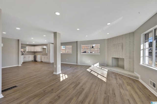 unfurnished living room with a brick fireplace, a healthy amount of sunlight, and light wood-type flooring