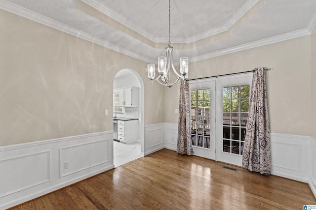 unfurnished dining area with a textured ceiling, wood-type flooring, a chandelier, ornamental molding, and a tray ceiling