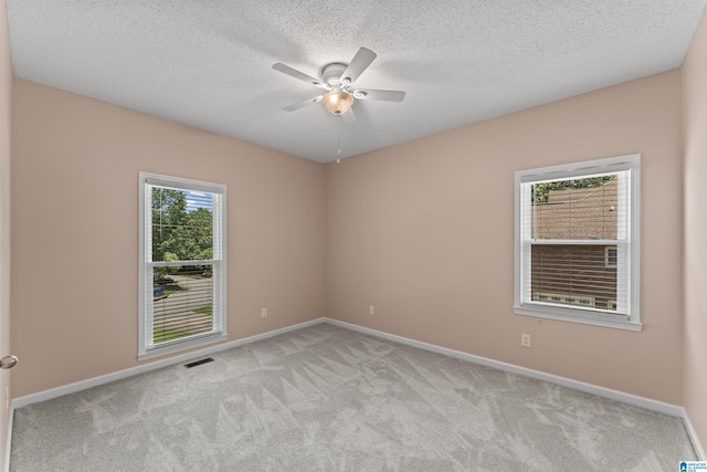 carpeted empty room with ceiling fan, a wealth of natural light, and a textured ceiling