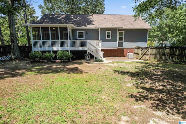 rear view of house with central AC unit, a sunroom, and a lawn