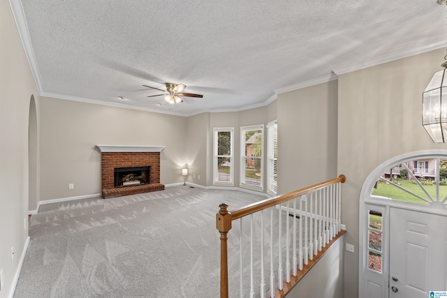 carpeted living room with a brick fireplace, ceiling fan with notable chandelier, ornamental molding, and a textured ceiling