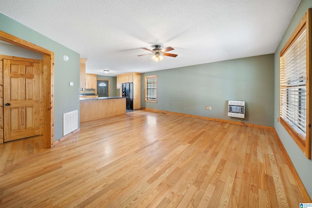 unfurnished living room featuring a textured ceiling, light hardwood / wood-style flooring, heating unit, and ceiling fan