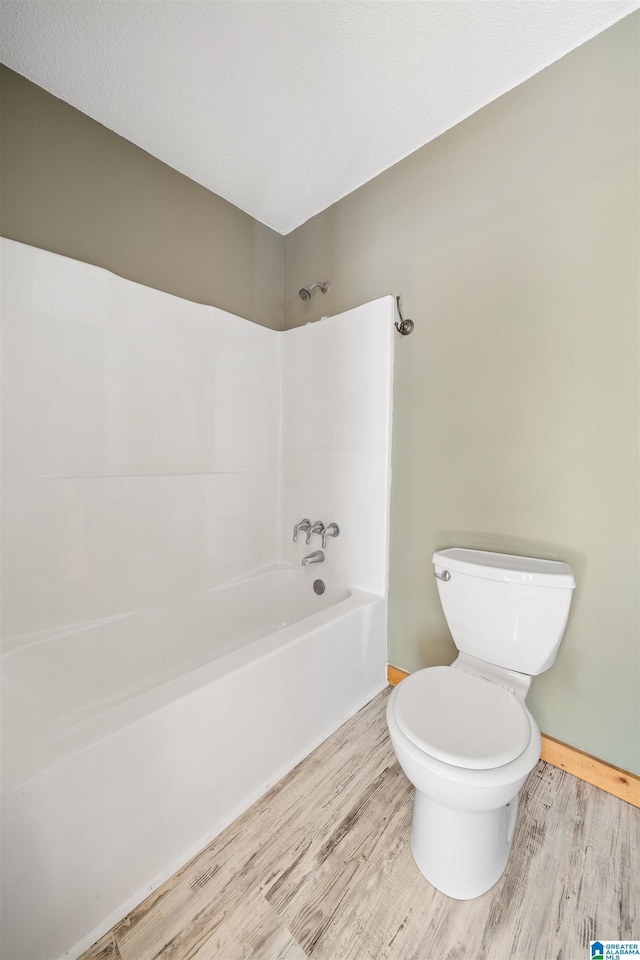 bathroom with hardwood / wood-style flooring, shower / bathing tub combination, and toilet