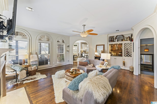 living room with built in shelves, a premium fireplace, dark hardwood / wood-style floors, ornamental molding, and ceiling fan