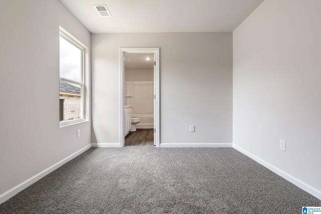 unfurnished bedroom with dark colored carpet and ensuite bathroom