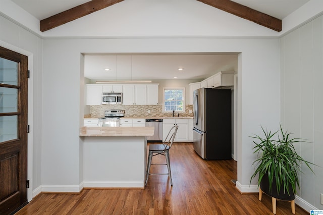 kitchen with a breakfast bar, kitchen peninsula, stainless steel appliances, decorative backsplash, and white cabinets