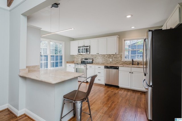 kitchen with pendant lighting, sink, stainless steel appliances, white cabinets, and kitchen peninsula