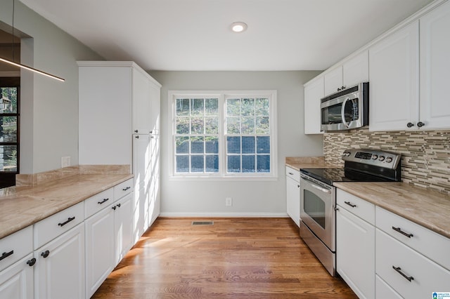 kitchen with white cabinets, backsplash, light stone counters, stainless steel appliances, and light wood-type flooring