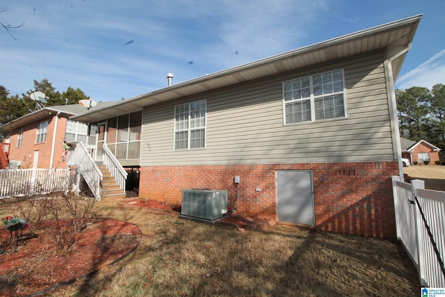 rear view of property featuring central air condition unit and a lawn