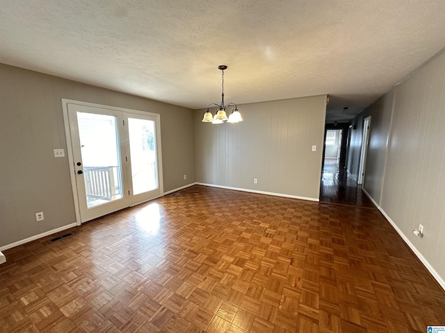 spare room featuring a textured ceiling, dark parquet flooring, and a notable chandelier