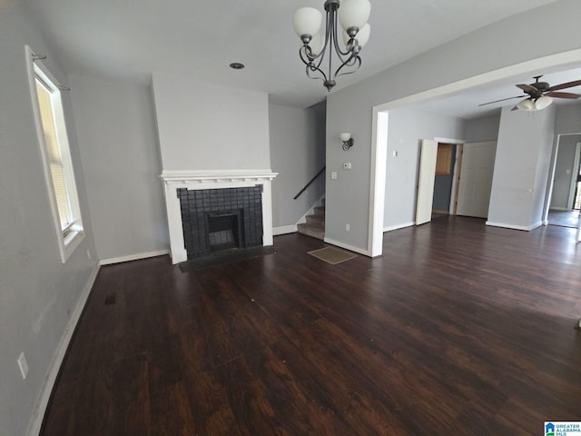 unfurnished living room featuring ceiling fan with notable chandelier, a wealth of natural light, dark wood-type flooring, and a tiled fireplace