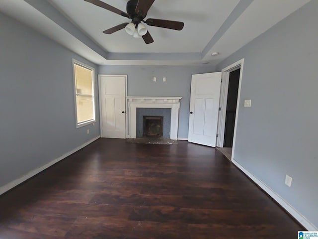 unfurnished living room featuring dark wood-type flooring, ceiling fan, and a raised ceiling