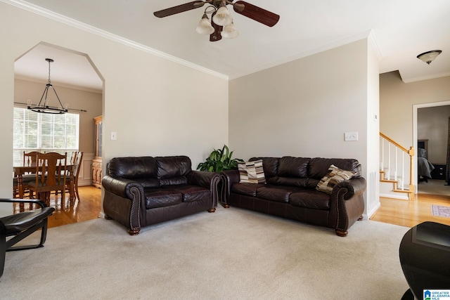 carpeted living room with ornamental molding and ceiling fan with notable chandelier